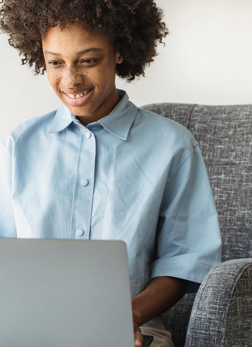 Happy teenager with curly hair in a blue shirt using a laptop indoors, showcasing joyful engagement.